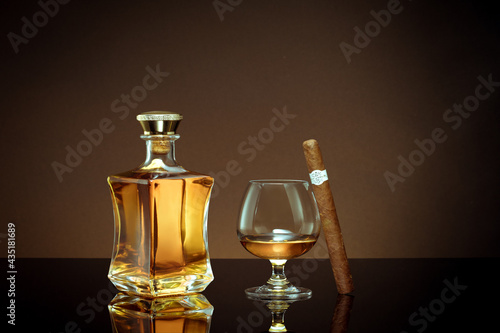 close up view of cigar, bottle of cognac and a glass aside on color back. 