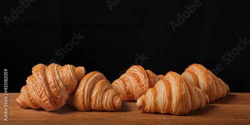 Heap of Fresh croissant on wooden board on black background.