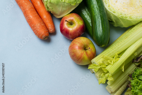 layout of vegetables on blue background: carrots, celery, cucumbers, zucchini, apples, cabbage, lettuce.  Concept of healthy eating. Vegan and vegetarian concept. Top view, place for text