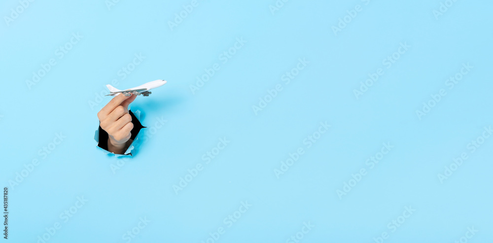 Business Hand holds model plane from a hole in the wall on blue background. insurance travel concept. Panoramic image Business Hand holds model plane from a hole in the wall on blue background. insurance travel concept. Panoramic image