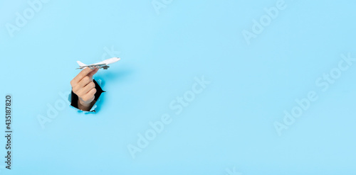 Business Hand holds model plane from a hole in the wall on blue background. insurance travel concept. Panoramic image