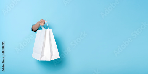 Woman hand holding paper shopping bag on blue banner background. Discounts and sale concept. Panoramic image