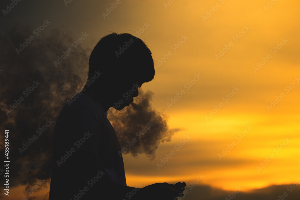 Man smoke electronic cigarette outdoor on beautiful sky background during sunset.