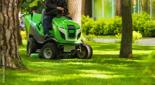 Professional worker trimming green grass with lawn mower m tractor in the park.