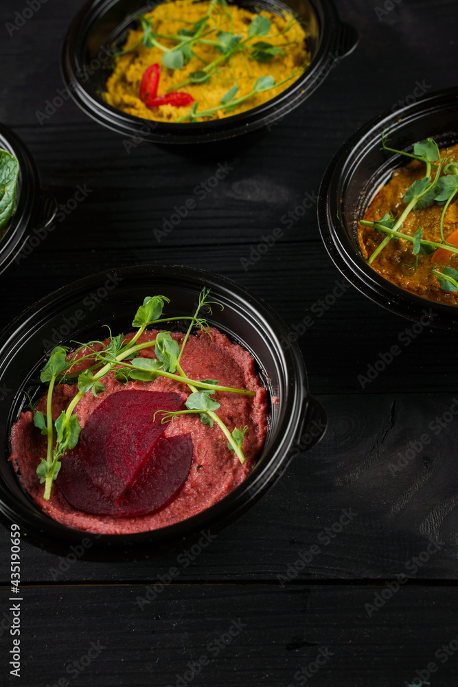 Hummus garnished peppers, chili, beet and herbs in black bowl on dark wooden table. Hummus assortment