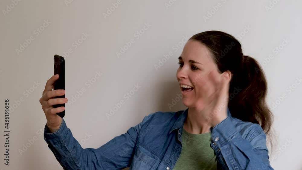 Young Caucasian woman on white background talks on video link using smartphone and looks at phone screen smiles rejoices and waves her hands. Important conversation over Internet online. 4K footage. Young Caucasian woman on white background talks on video link using smartphone and looks at phone screen smiles rejoices and waves her hands. Important conversation over Internet online. 4K footage.