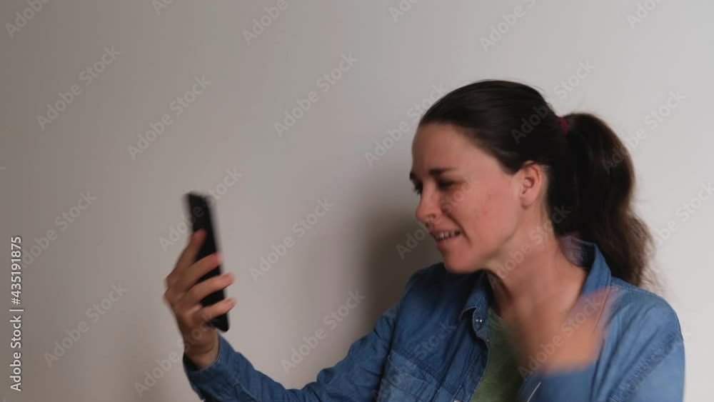 Young Caucasian European woman on white background talks on video link using smartphone and looks at phone screen smiles and blows kiss. 4K footage. Conversation over Internet with loved one. Young Caucasian European woman on white background talks on video link using smartphone and looks at phone screen smiles and blows kiss. 4K footage. Conversation over Internet with loved one.