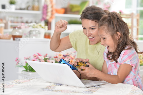 portrait of cute little girl with young mother playing computer game with laptop