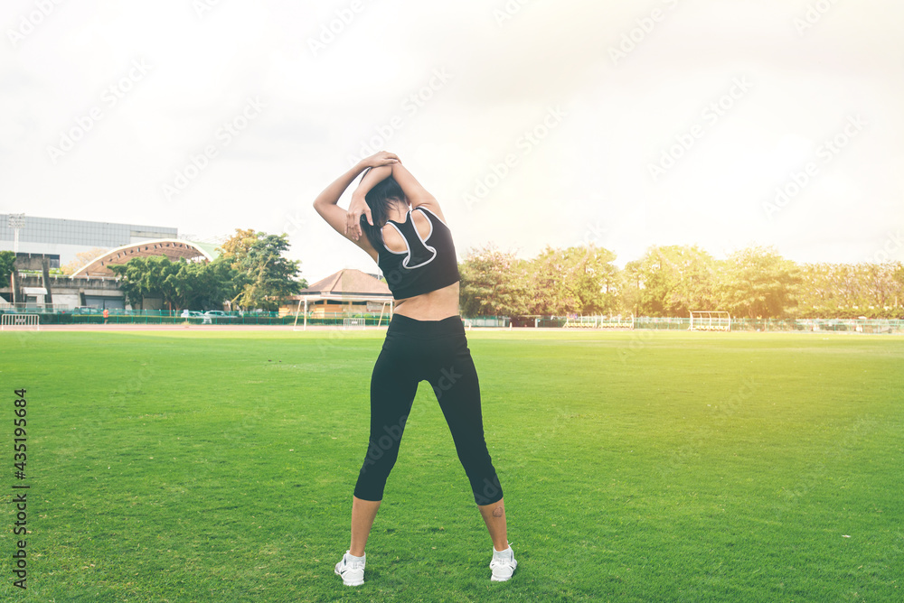Back of young woman exercising on green grass. female fitness model stretching exercise or warming up before work out. exercise, Fitness, workout, sport, lifestyle concept. Back of young woman exercising on green grass. female fitness model stretching exercise or warming up before work out. exercise, Fitness, workout, sport, lifestyle concept.