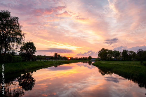 Beautiful setting sun with colored clouds and the reflections in the water of the river called "the Dinkel" in purple, magenta, yellow, orange and blue. Region of Twente, province of Overijssel