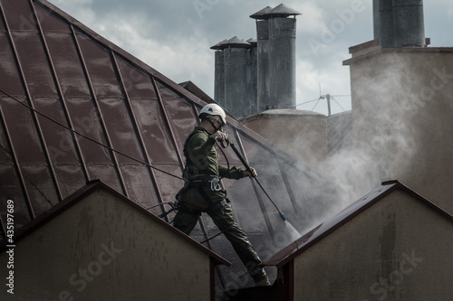 a man washing a roof with pressurized water work at a height. cleaning services protection of a worker working at a height