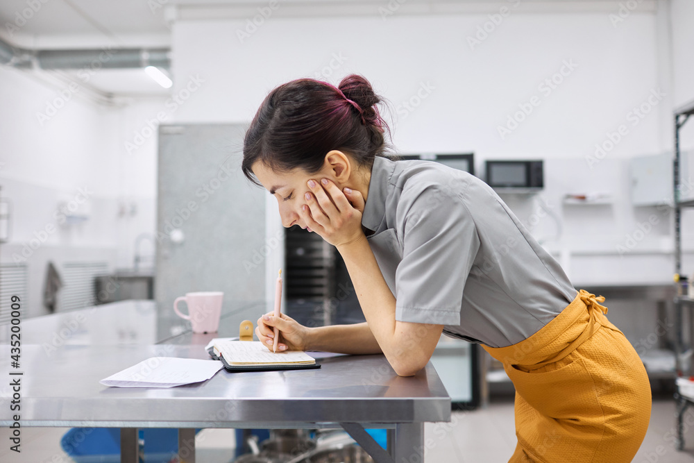 The pastry chef girl makes notes in a notebook. The pastry chef girl makes notes in a notebook.