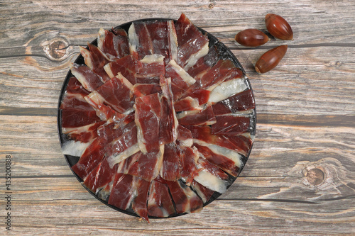 Portion of 100% acorn-fed Iberian ham Dehesa de Extremadura decorated with acorns on wooden background