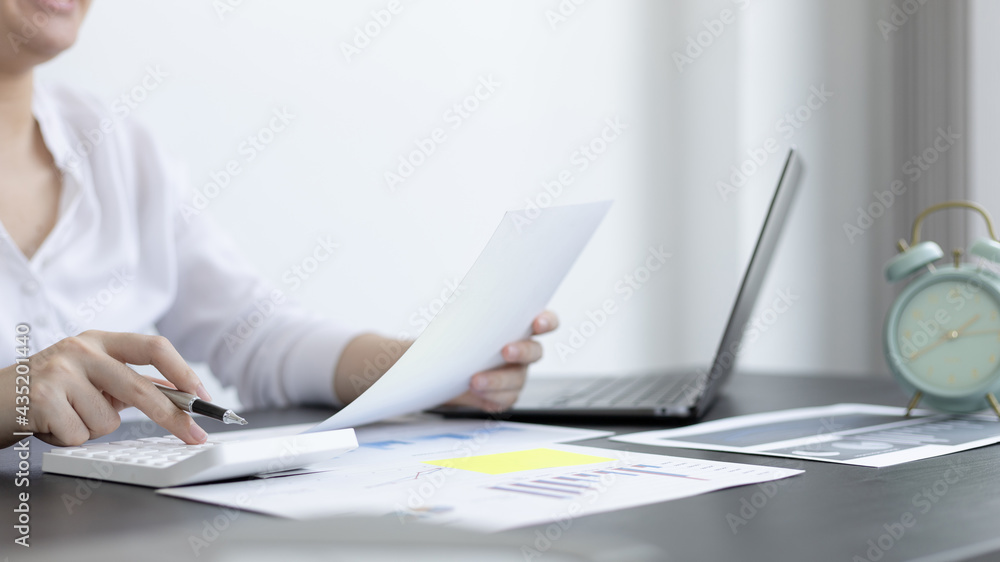 Young Asian businesswoman presses a calculator to calculate income tax and corporate income in a private office, Finance, Accounting, Tex, Statistical graphs of marketers investing in real estate. Young Asian businesswoman presses a calculator to calculate income tax and corporate income in a private office, Finance, Accounting, Tex, Statistical graphs of marketers investing in real estate.