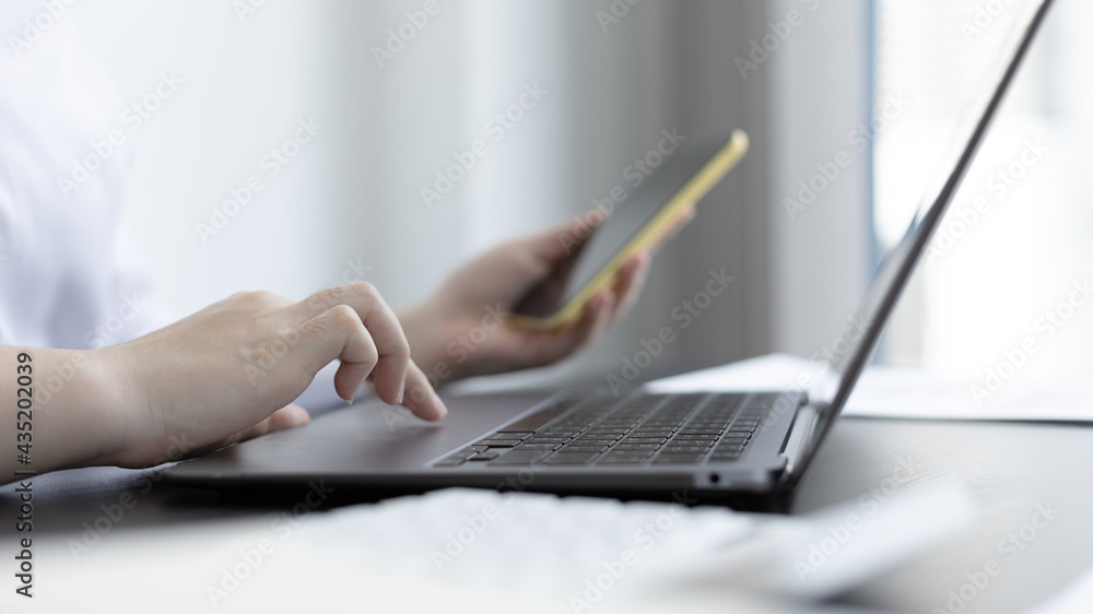 Finance workers are reviewing the company's financial data on a laptop and using smartphones to communicate or chat with the team at social distances, Working alone in a private office.