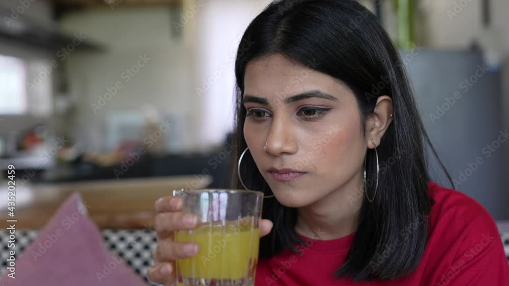 Cropped view of pretty tired young Asian woman looking to the side and drinking juice while resting at home.attractive concentrated young lady drinking juice feel unhappy and frustrated at home. Cropped view of pretty tired young Asian woman looking to the side and drinking juice while resting at home.attractive concentrated young lady drinking juice feel unhappy and frustrated at home.