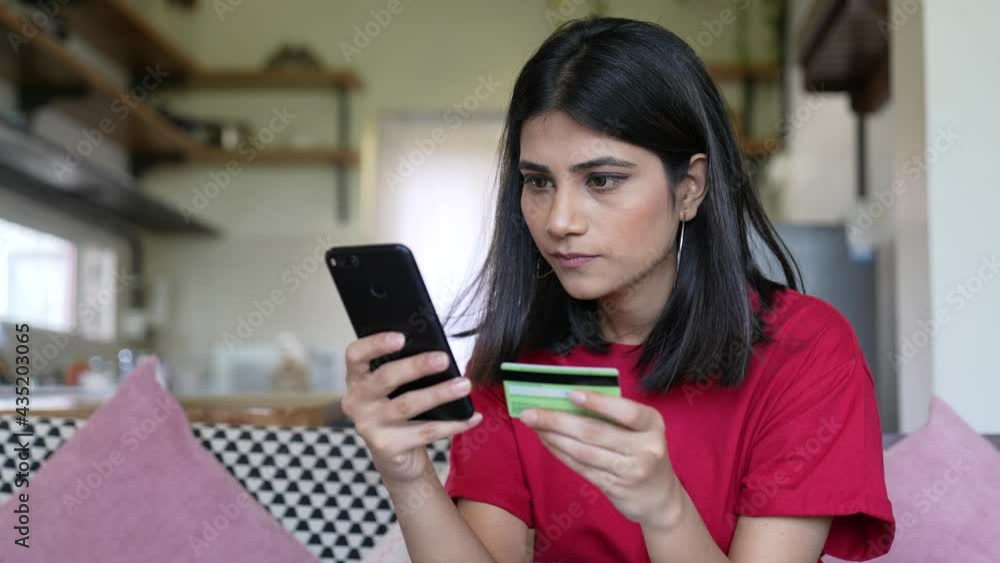 Young Asian woman holding a credit card and using smart phone for make an online shopping payment at home indoor.lifestyle concept.happy lady holding her smart phone is typing credit card numbers. Young Asian woman holding a credit card and using smart phone for make an online shopping payment at home indoor.lifestyle concept.happy lady holding her smart phone is typing credit card numbers.