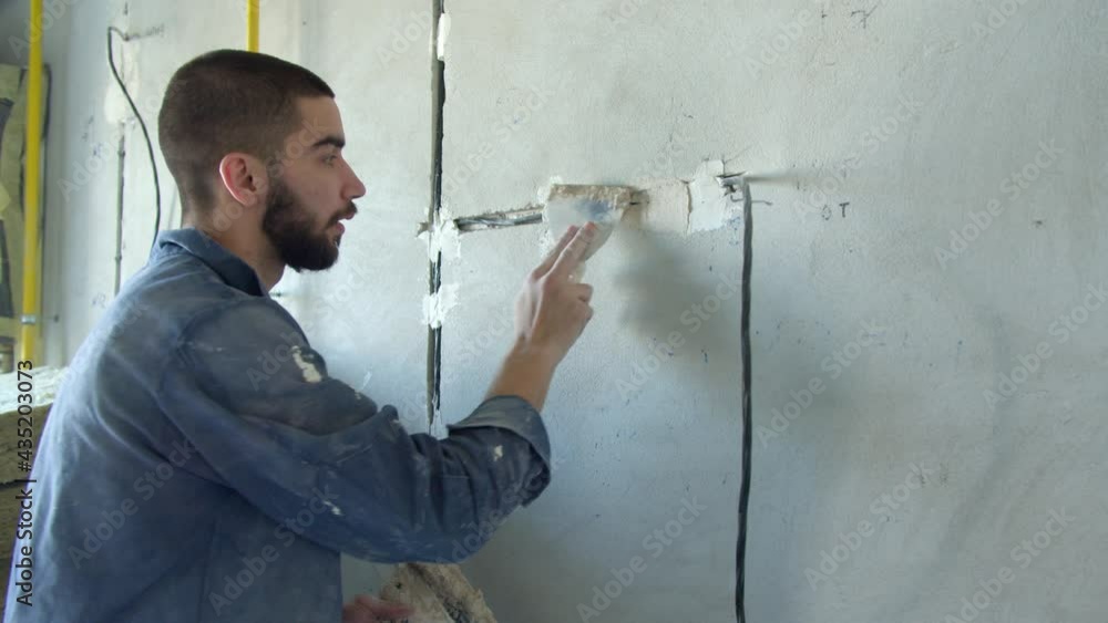 Bearded contractor spreading plaster on wire trunking Bearded contractor spreading plaster on wire trunking
