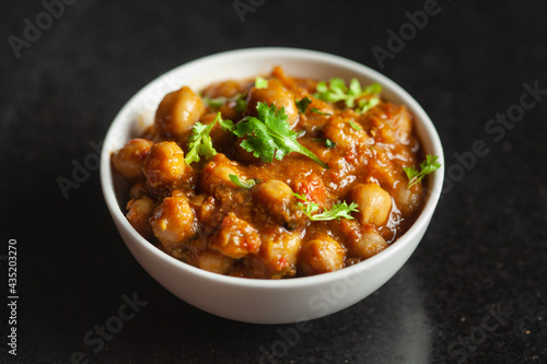 Chickpeas masala (Spicy chola or chhole curry) garnished with fresh green coriander and ingredients. Served in a ceramic bowl. An Classic Indian typical Panjabi street food. 