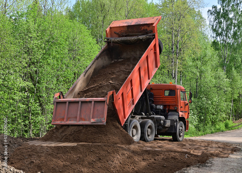 Fotografi A truck unloads sand on a country road to level and repair the pavement