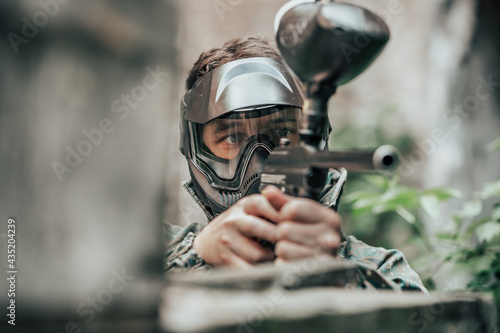 Young man playing paintball battle game with his friends, wearing a camouflage and protective mask, banner, leisure activity