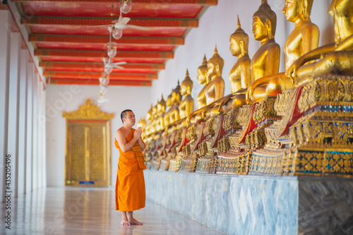 Monk walking down the hallway with buda statues around him
