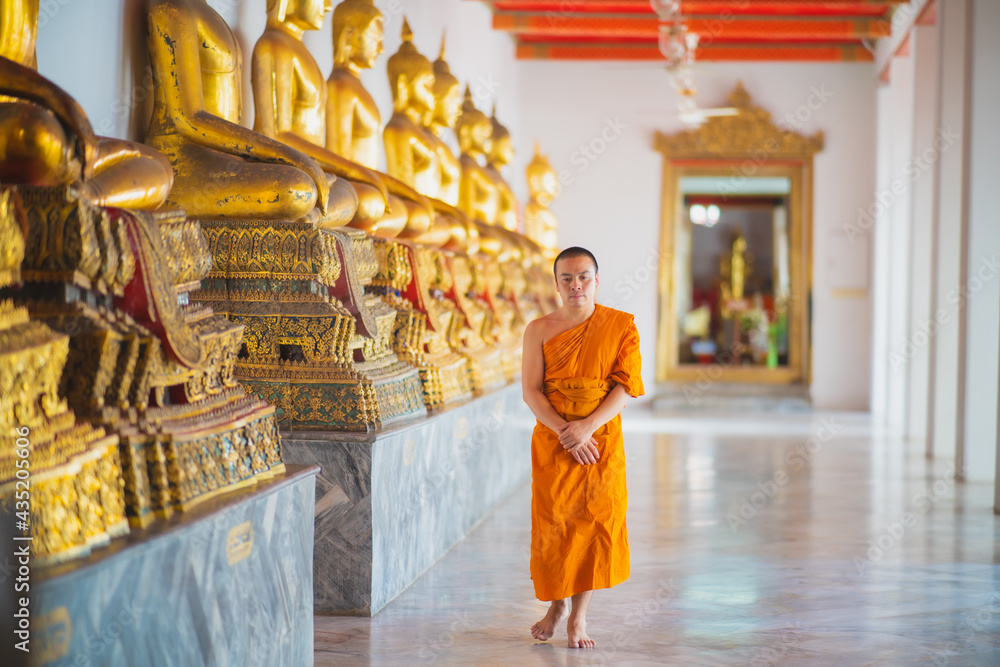 Fototapeta premium Monk walking down the hallway with buda statues around him