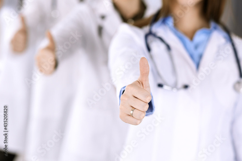 Group of modern doctors standing as a team with thumbs up in hospital office. Medical help, insurance in health care, best desease treatment and medicine concept