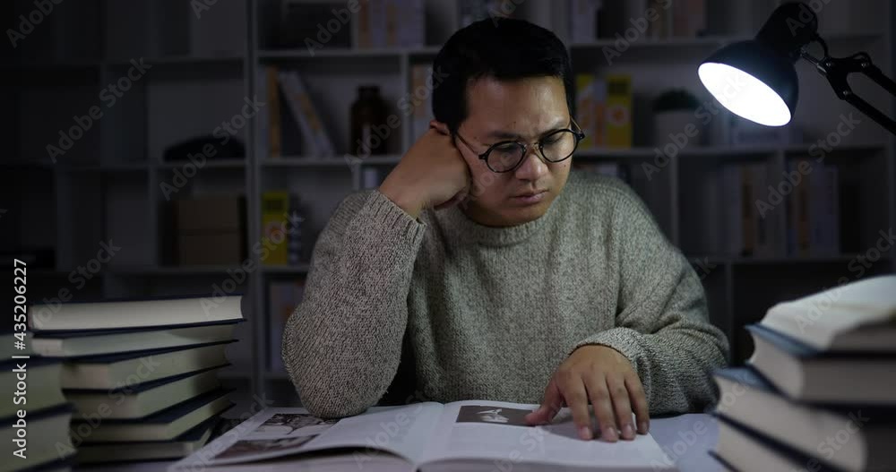 young man sitting and reading book in dimly lit library young man sitting and reading book in dimly lit library