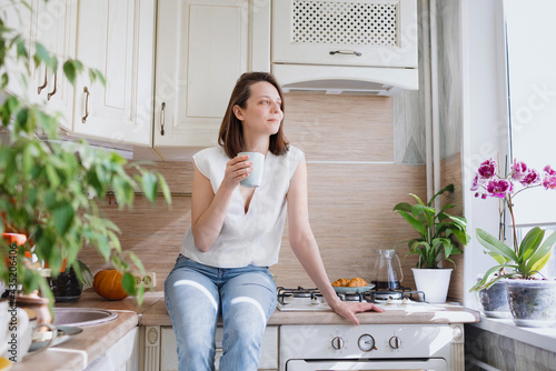 a European woman sits on the table in her kitchen and drinks coffee, breakfast in the kitchen coffee and croissant, internet detox and rest in the morning, calm and measured breakfast, rest and time