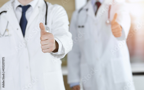 Group of unknown doctors standing as a team with thumbs up or Ok sign in hospital office, close-up. Medical help, insurance in health care, best treatment and medicine concept