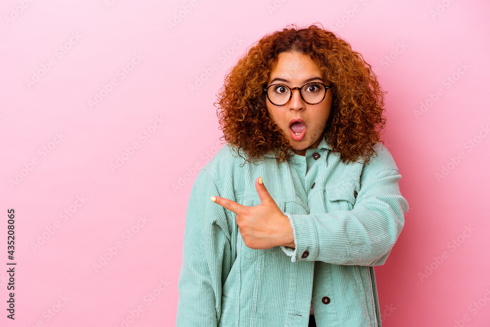 Fototapeta premium Young latin curvy woman isolated on pink background smiling and pointing aside, showing something at blank space.