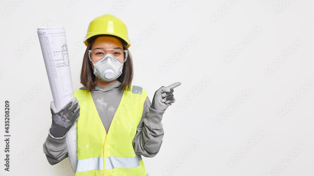 Asian female engineer wears safety helmet protective gloves and mask holds building blueprints indicates away on blank space shows project isolated over white background shows results of work