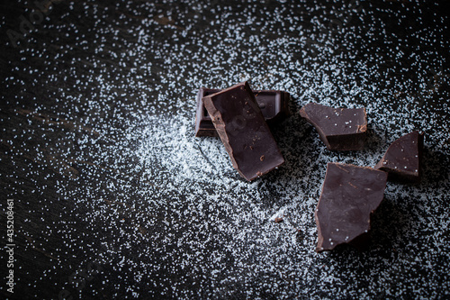 A close up of dark chocolate squares with sugar on a dark wooden table.