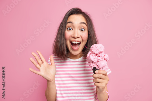 Quadro su tela Emotional brunette woman exlaims loudly keeps palm raised eats delicious ice cre