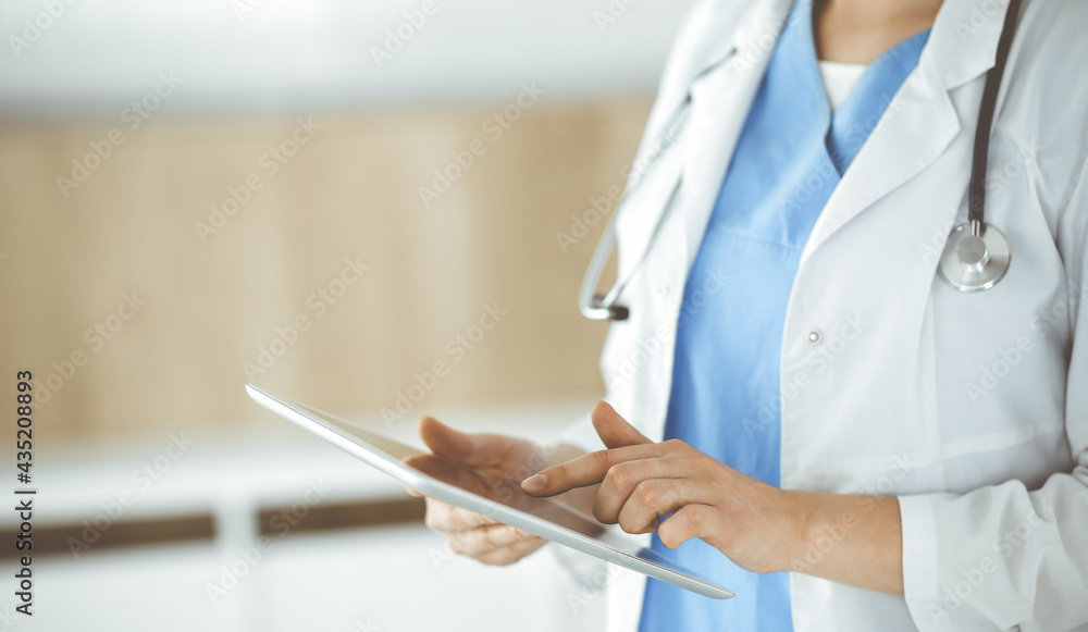 Unknown woman-doctor standing in clinic and using tablet pc, close-up. Data in medicine and healthcare Unknown woman-doctor standing in clinic and using tablet pc, close-up. Data in medicine and healthcare