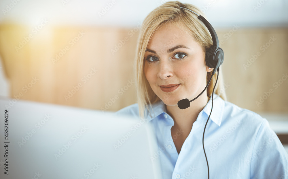 Blonde business woman sitting and communicated by headset in call center in sunny office. Concept of telesales business Blonde business woman sitting and communicated by headset in call center in sunny office. Concept of telesales business