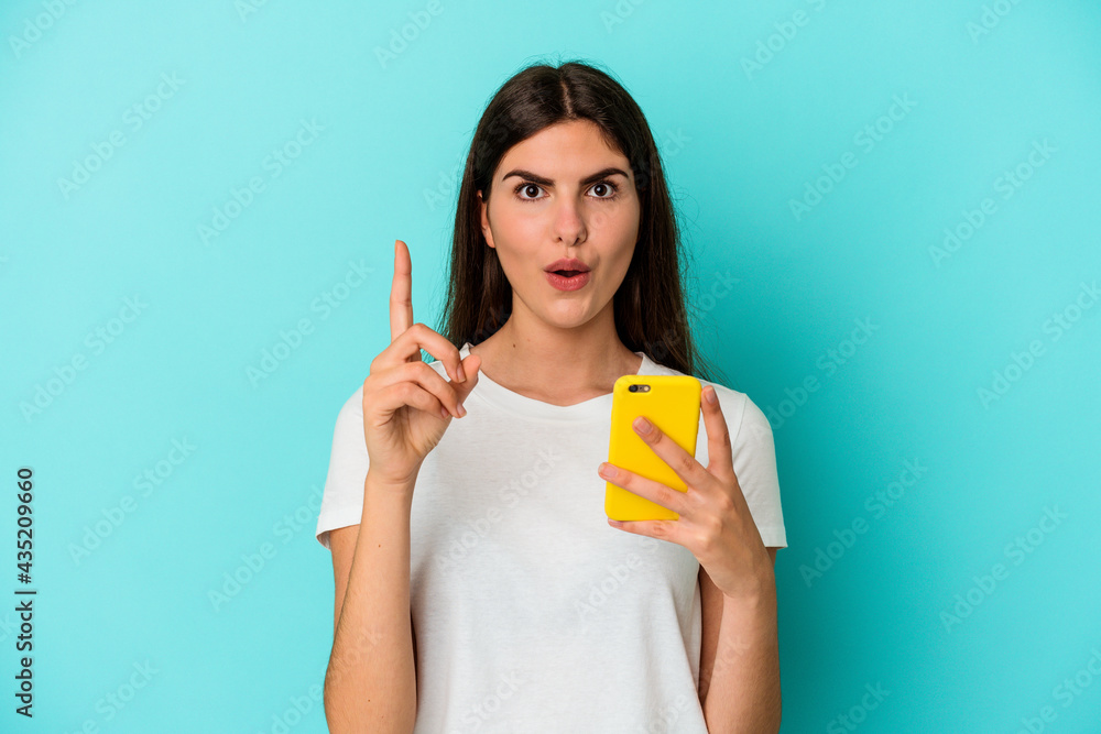 Young caucasian woman holding a mobile phone isolated on blue background having some great idea, concept of creativity. Young caucasian woman holding a mobile phone isolated on blue background having some great idea, concept of creativity.
