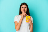 Young caucasian woman holding a mobile phone isolated on blue background keeping a secret or asking for silence.