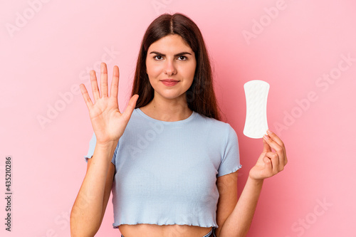 Young caucasian woman holding a compress isolated on pink background smiling cheerful showing number five with fingers.