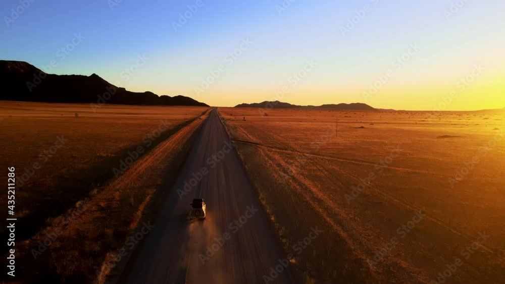 Drone shot from front of suv travelling through african desert. Aerial view of car with tourists moving through orange sand plain. Incredible background of hills and setting sun shot by drone. Drone shot from front of suv travelling through african desert. Aerial view of car with tourists moving through orange sand plain. Incredible background of hills and setting sun shot by drone.