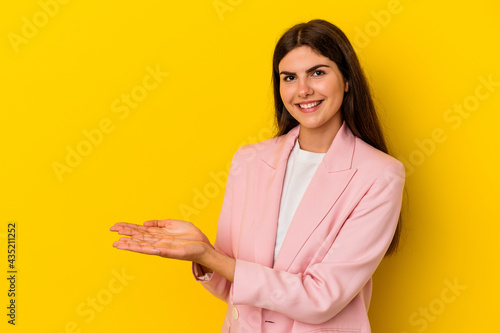 Young caucasian woman isolated on yellow background holding a copy space on a palm. © Asier