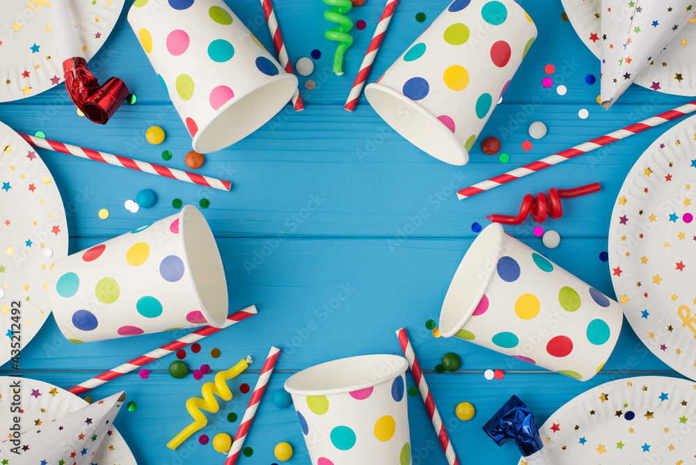 Obraz premium Top view photo of party table decoration paper plates cups hats pipes straws spiral candles sequins and confetti on isolated blue wooden table background with blank space