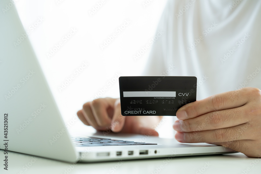 Unrecognizable Asian young man using a credit card for making a purchase on the internet. Unrecognizable Asian young man using a credit card for making a purchase on the internet.
