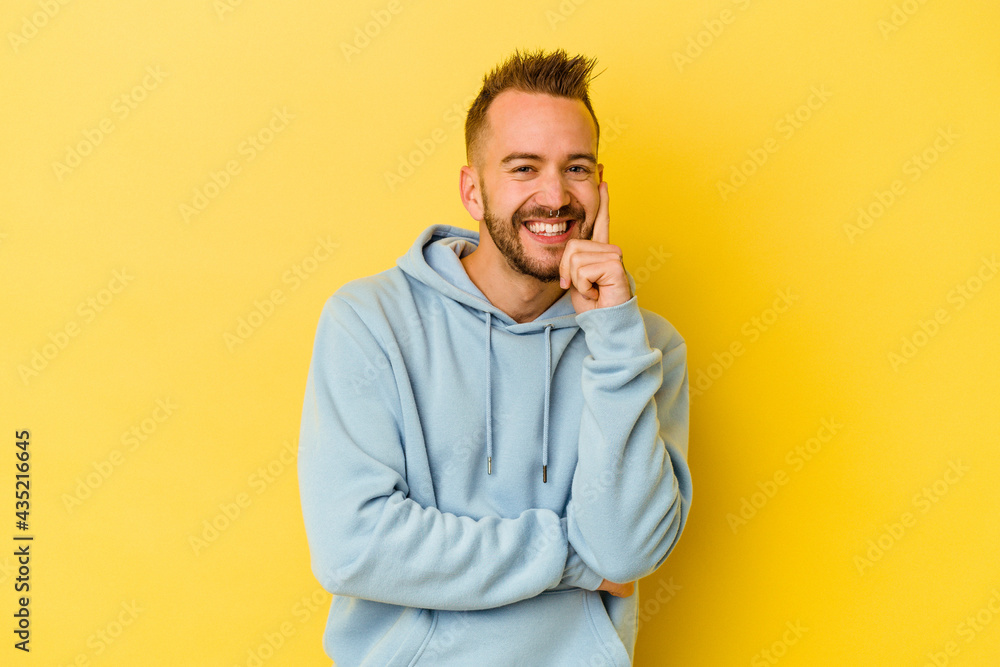Young tattooed caucasian man isolated on yellow background smiling happy and confident, touching chin with hand. Young tattooed caucasian man isolated on yellow background smiling happy and confident, touching chin with hand.