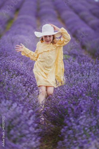 Smiling small girl in yellow dress and white hat running in a lavender field