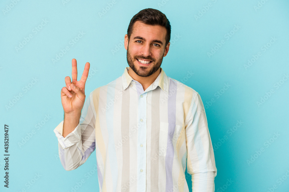 Naklejka premium Young caucasian man isolated on blue background showing victory sign and smiling broadly.