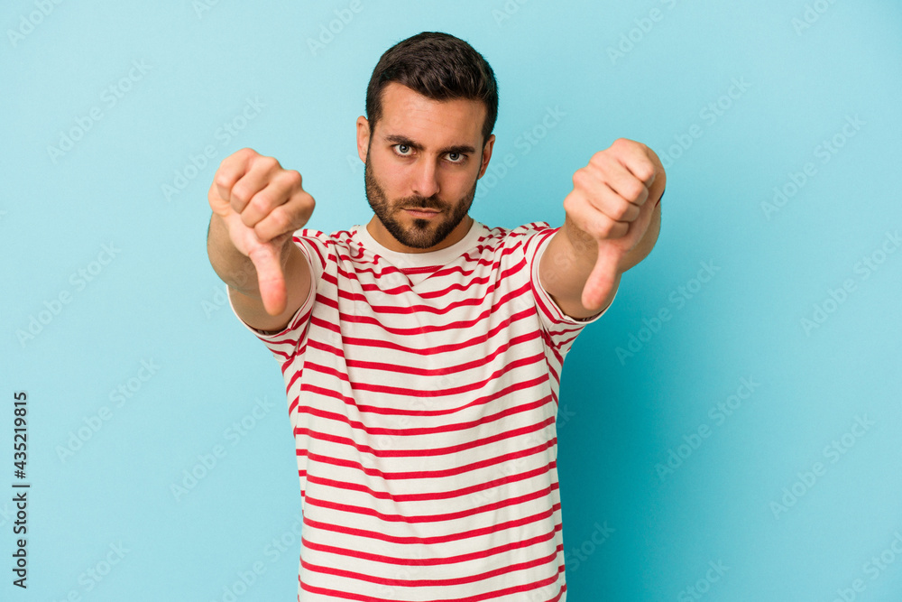 Young caucasian man isolated on blue background showing thumb down and expressing dislike. Young caucasian man isolated on blue background showing thumb down and expressing dislike.