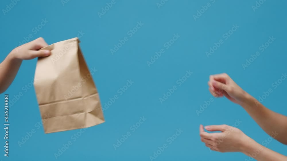 Young woman hand hold brown clear empty blank craft paper bag food for takeaway over blue background. Copy space for place a text for advertisement. Advertising area, mock up promotional content. Young woman hand hold brown clear empty blank craft paper bag food for takeaway over blue background. Copy space for place a text for advertisement. Advertising area, mock up promotional content.