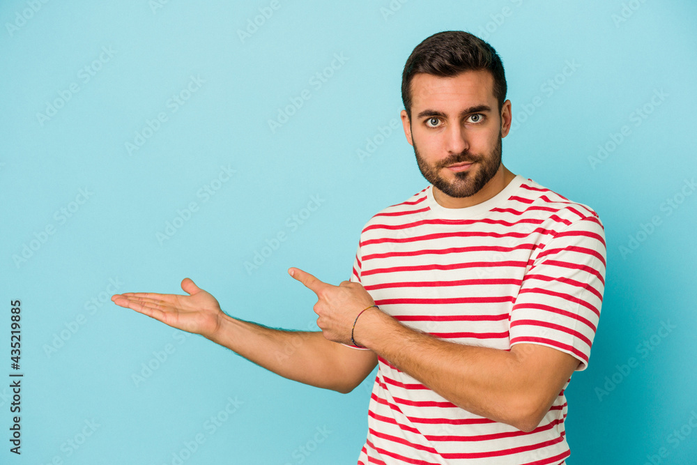 Fototapeta premium Young caucasian man isolated on blue background excited holding a copy space on palm.